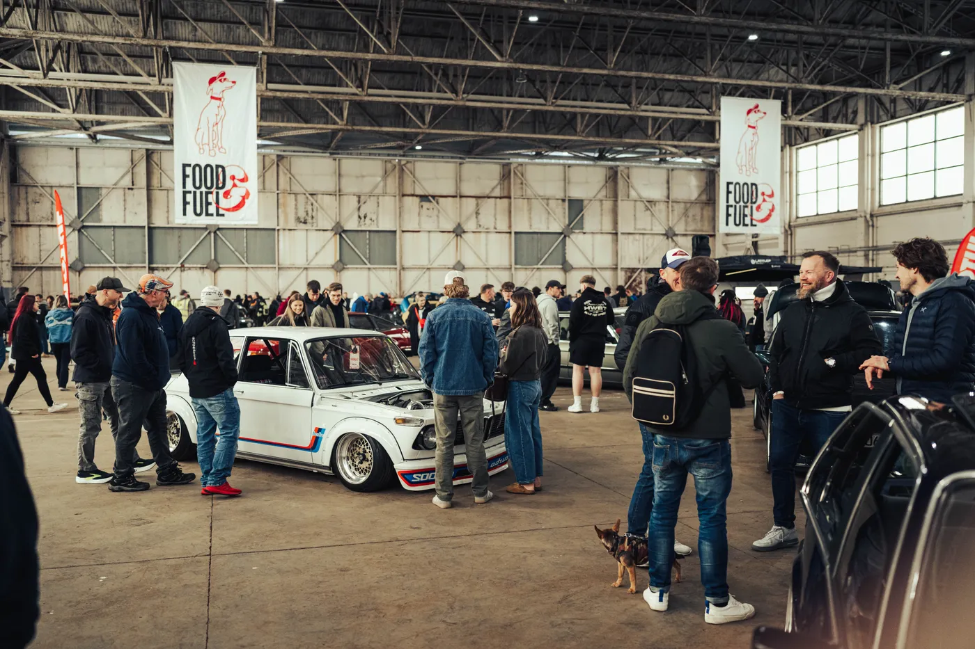 Visitors gathered around a modified BMW 2002 inside a hangar at Food&Fuel, under Food&Fuel banners